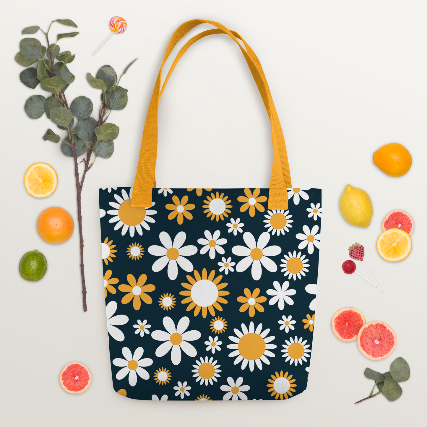 Polyester tygväska med gula handtag och ett heltäckande mönster av vita och gula prästkragar på mörkblå bakgrund.
Polyester tote bag with yellow handles and an all-over print of white and yellow daisies on a dark blue background.