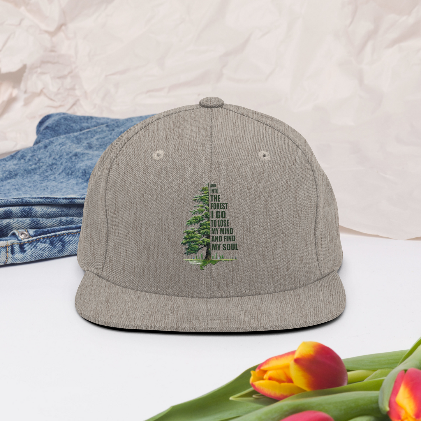 Melerad grå snapback-keps med broderat granmotiv som bildar citatet ”And into the forest I go to lose my mind and find my soul”.
Heather gray snapback cap, featuring embroidered pine tree artwork forming the quote “And into the forest I go to lose my mind and find my soul”.
