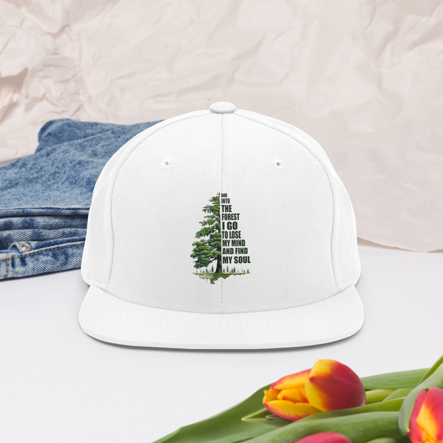 Vit snapback-keps med broderat granmotiv som bildar citatet ”And into the forest I go to lose my mind and find my soul”.
White snapback cap, featuring embroidered pine tree artwork forming the quote “And into the forest I go to lose my mind and find my soul”.