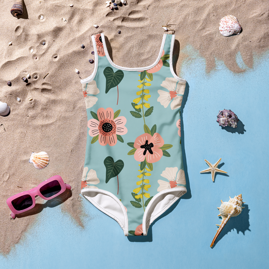 Flicka i blommig baddräkt med akvarellmönster i rosa, vitt och grönt mot blå bakgrund.
Girl in a floral swimsuit with a watercolor pattern in pink, white, and green against a blue background.