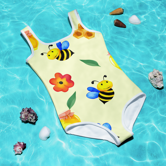 Barnbaddräkt med söta bin, blommor och honung på ljusgul bakgrund.
Kids' swimsuit with cute bees, colorful flowers, and honey jars on a light yellow background.