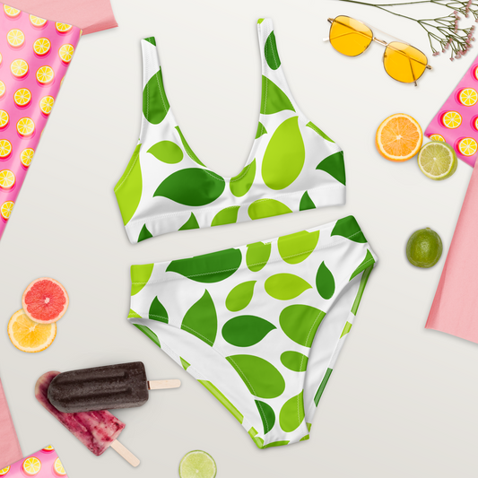 Högmidjad bikini i återvunnet material med stora stiliserade gröna blad på vit bakgrund.
High-waisted bikini made from recycled material with bold stylized green leaves on a white background.