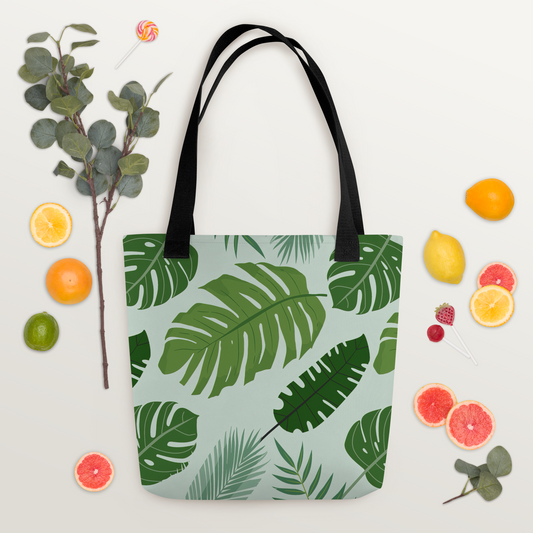 Polyester-tygväska med svart handtag och tropiskt bladmotiv i gröna nyanser på ljus bakgrund.
Polyester tote bag with black handle and tropical leaf pattern in green tones on a light background.