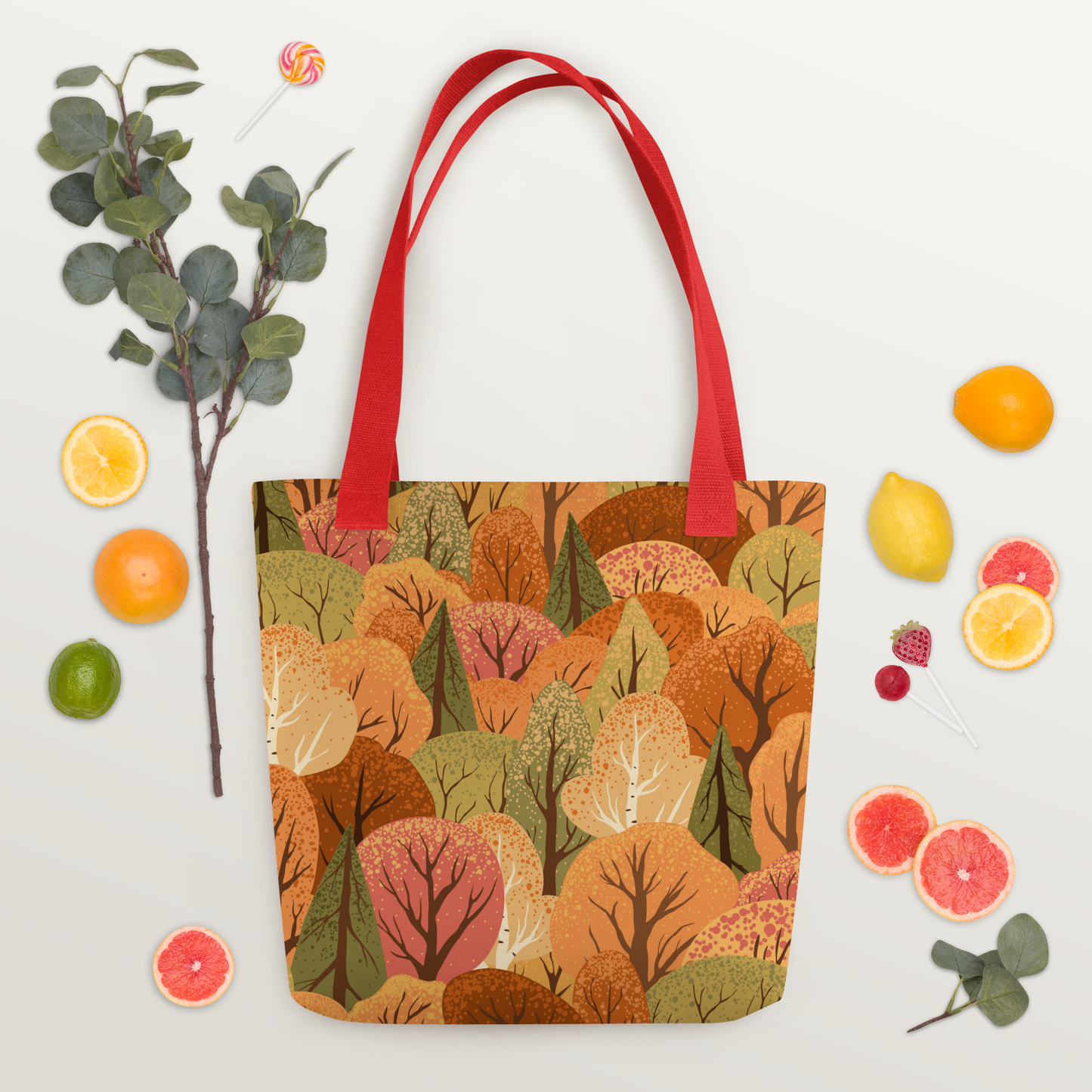 Polyester-tygväska med rött handtag och mönster av stiliserade träd i höstens färger – orange, rött, gult och grönt.
Polyester tote bag with red handle and a stylized pattern of autumn-colored trees in orange, red, yellow, and green.