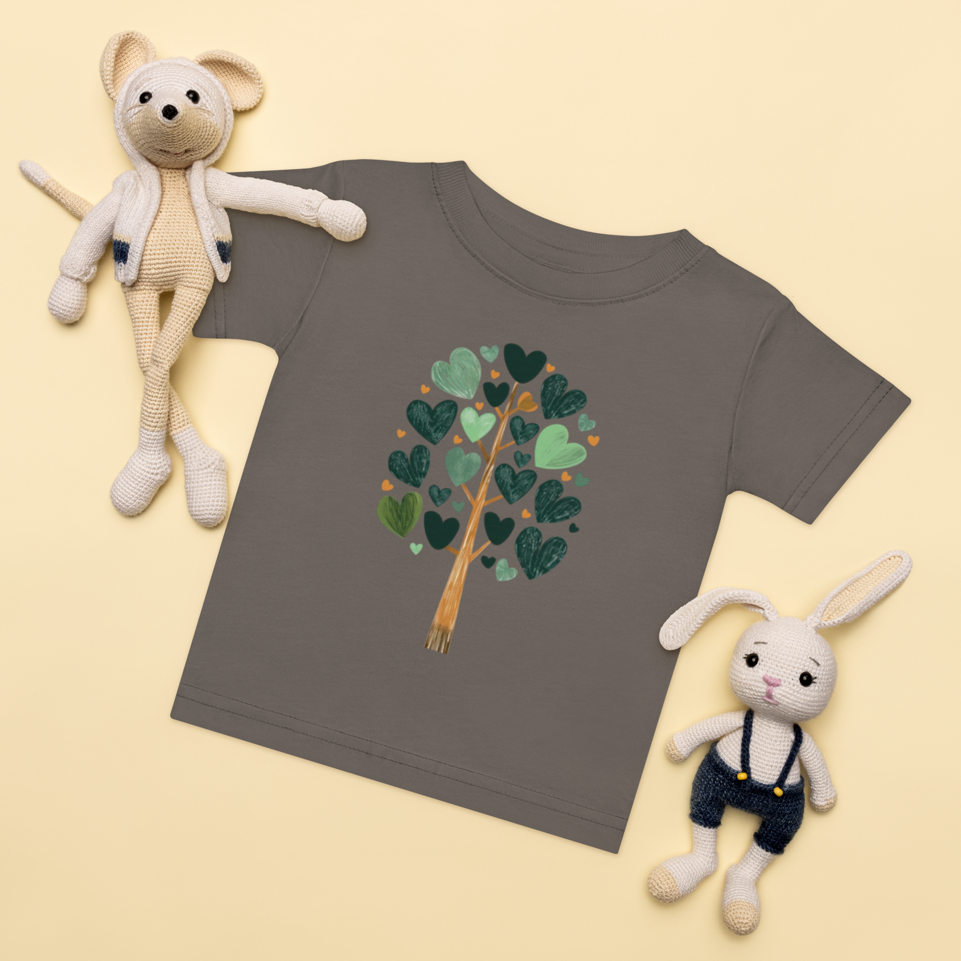 Baby-t-shirt i mörkgrå med ett träd av gröna hjärtan framtill.
Baby t-shirt in charcoal with a heart-shaped leaf tree illustration on the front.
