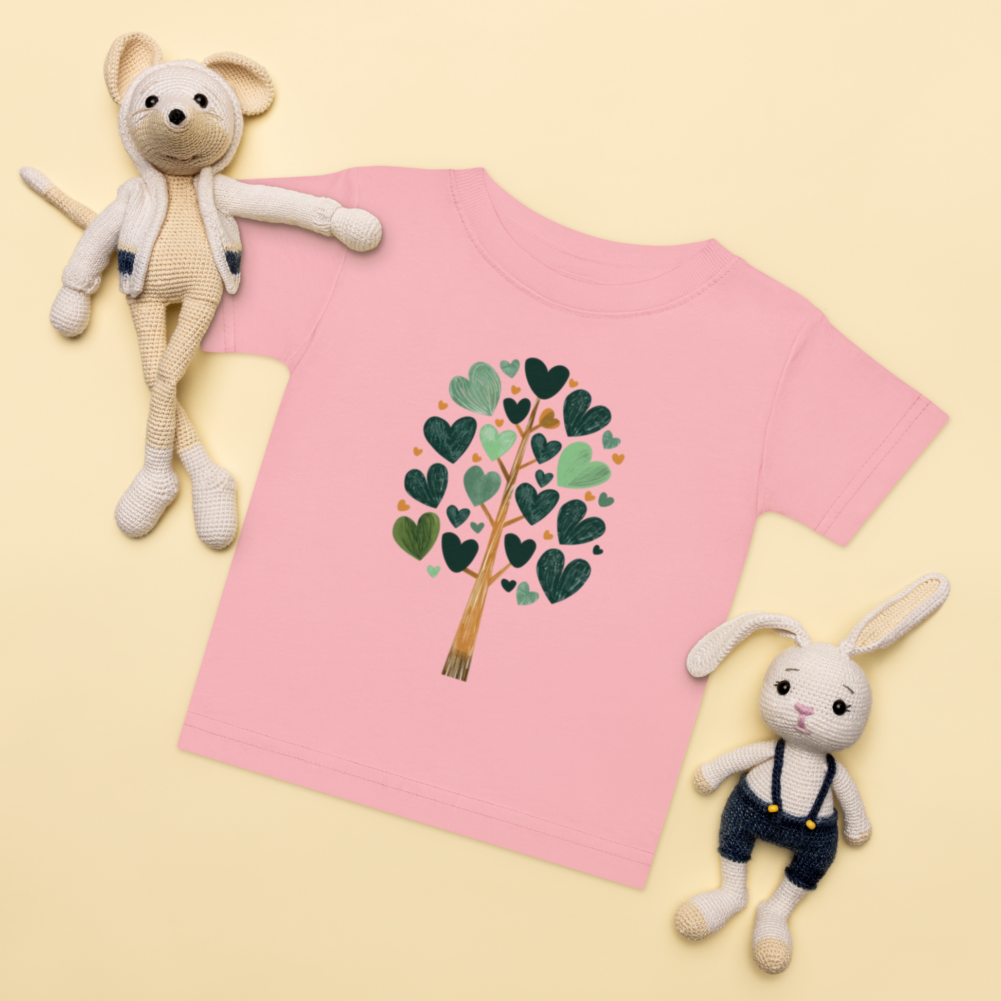 Baby-t-shirt i rosa med ett träd av gröna hjärtan framtill.
Baby t-shirt in pink with a heart-shaped leaf tree illustration on the front.