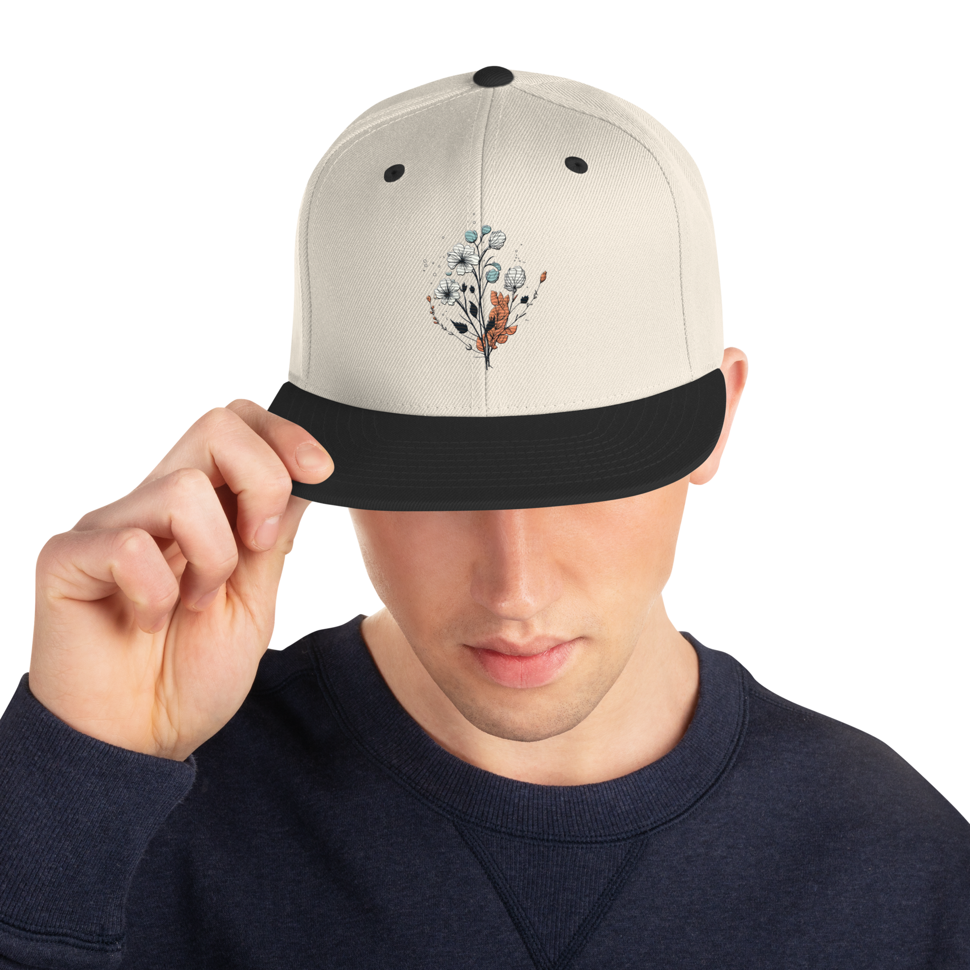 Natur snapback keps med svart skärm och broderad blomdesign framtill.
Natural snapback cap with black brim and embroidered floral design on the front.