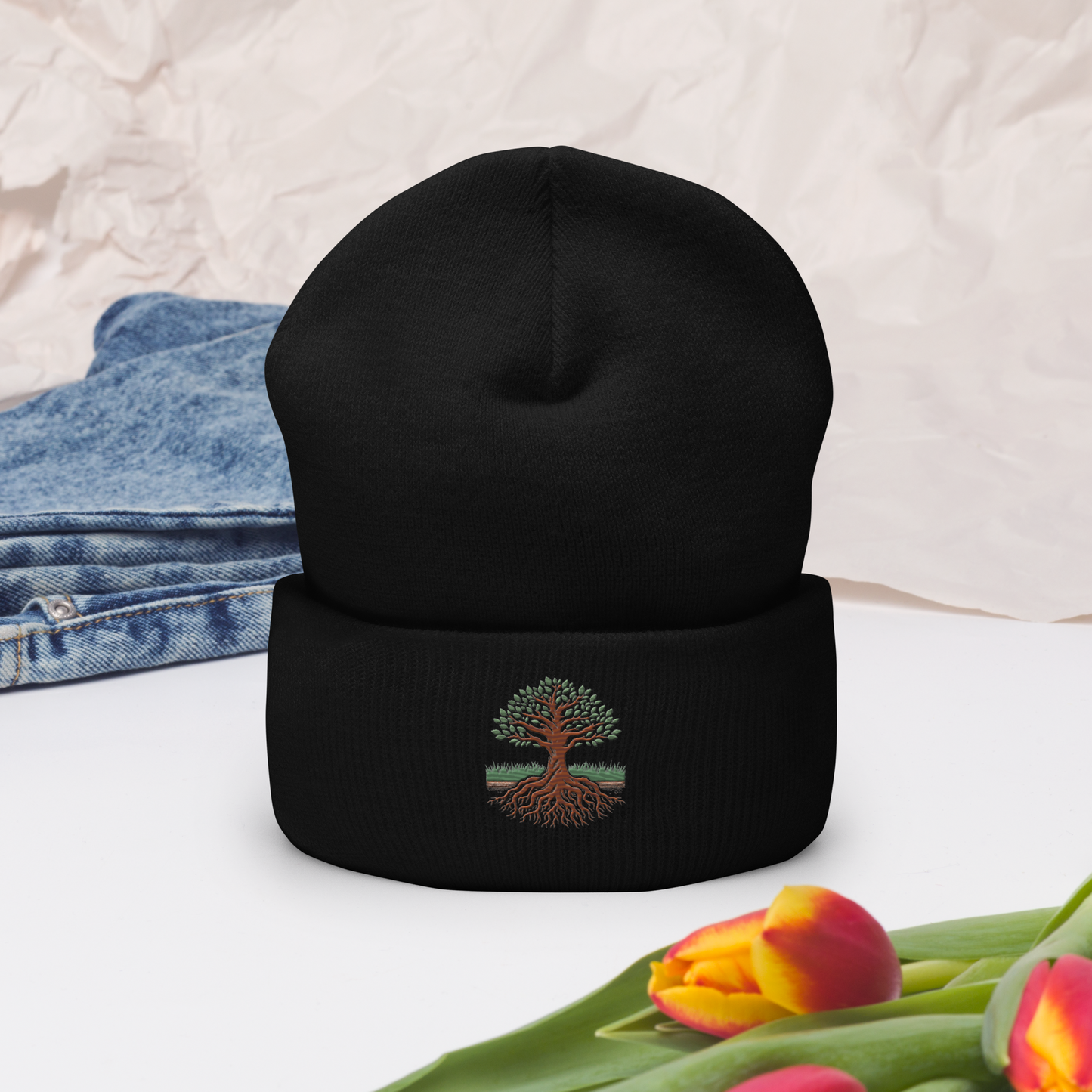 Svart uppvikt mössa med broderat träd och rötter i grönt och brunt framtill.
Black cuffed beanie with embroidered tree and roots in green and brown on the front.