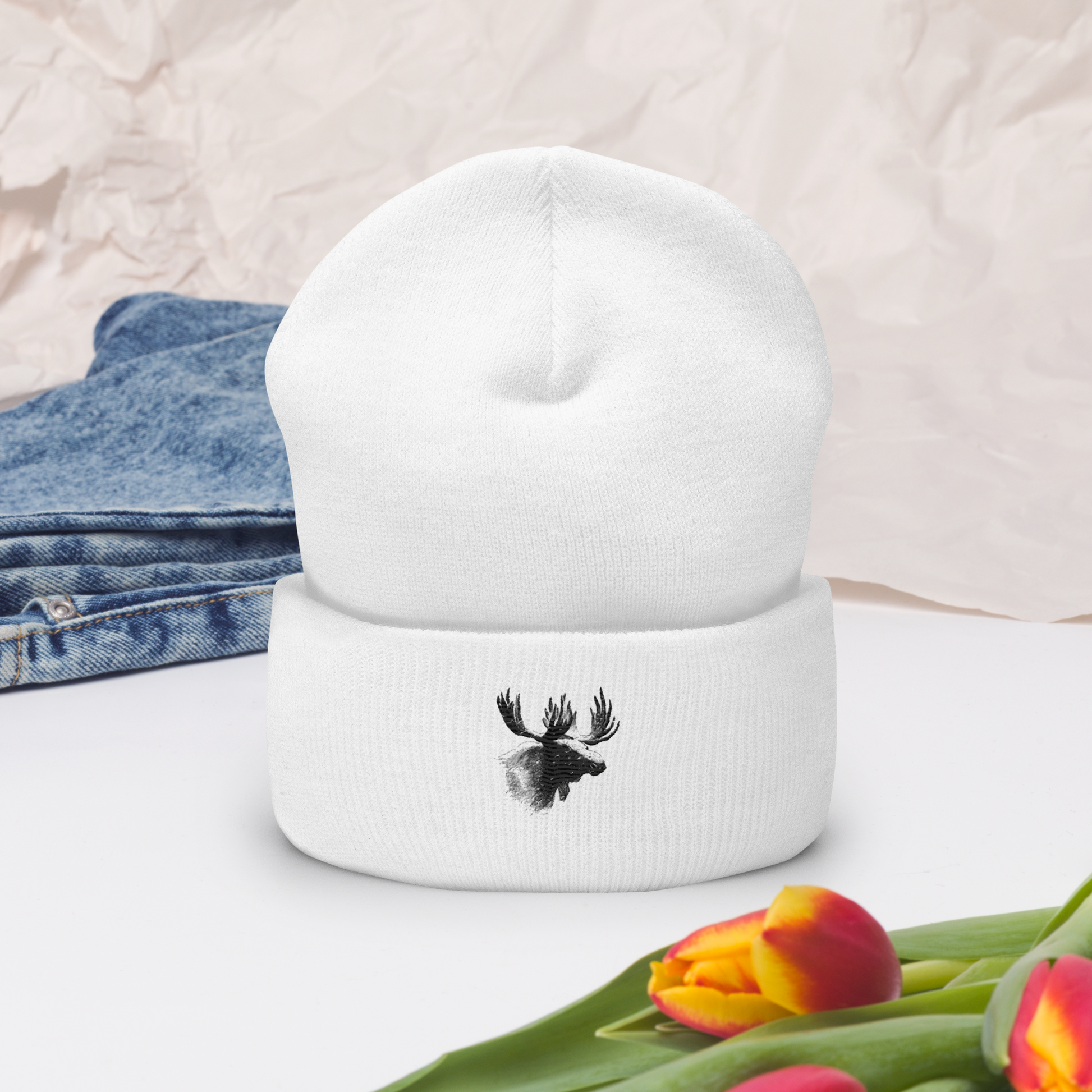 Vit uppvikt mössa med broderat älghuvud i svart framtill.
White cuffed beanie with black embroidered moose head on the front.