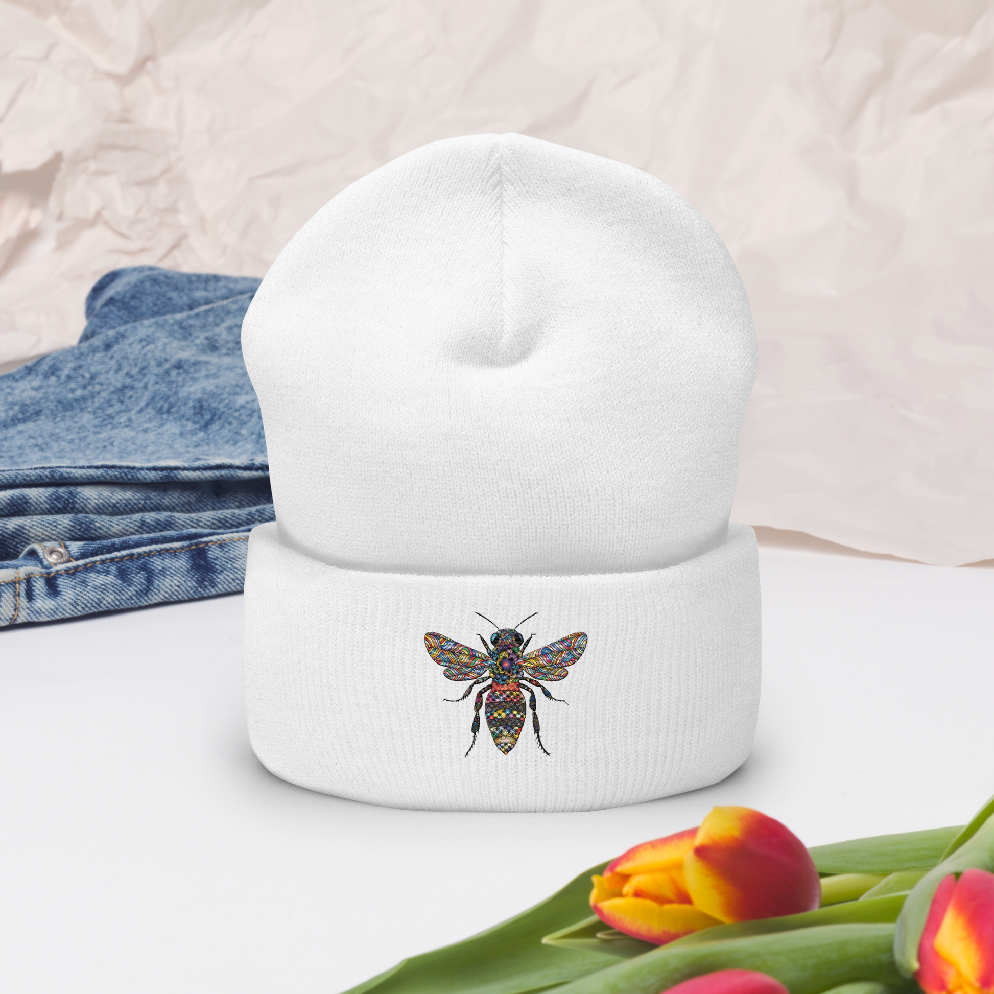 Vit uppvikt mössa med broderad bi i flerfärg framtill.
White cuffed beanie with multicolored embroidered bee on the front.