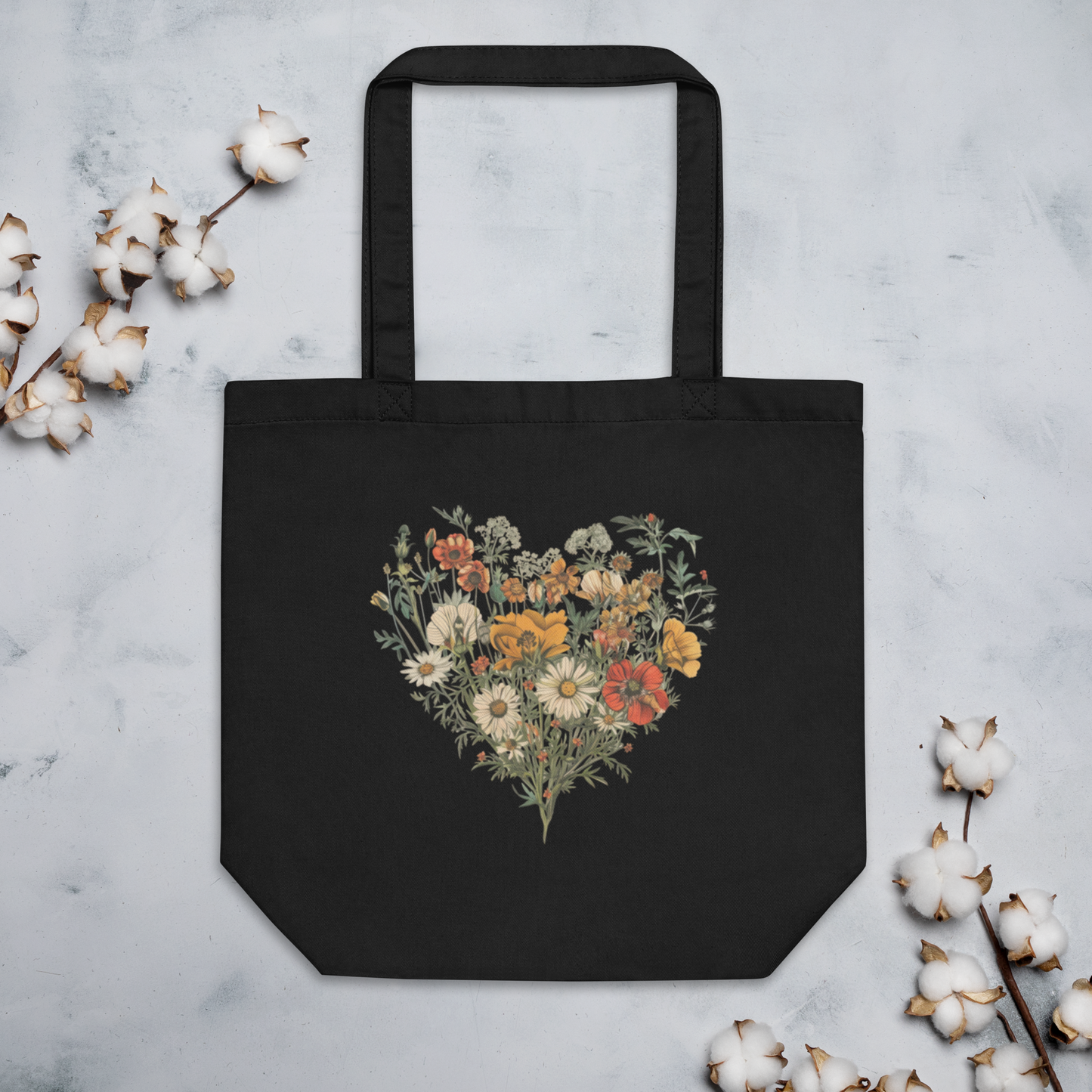 Svart ekologisk tygväska med ett hjärta av färgglada vilda blommor tryckt i mitten.
Black organic tote bag featuring a heart made of colorful wildflowers printed in the center.