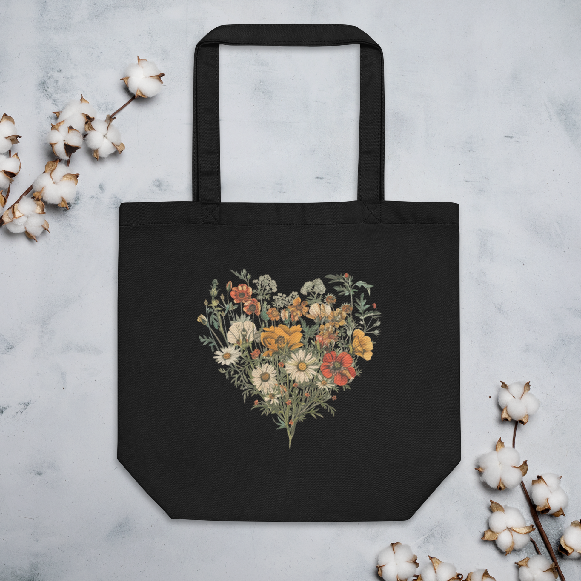 Svart ekologisk tygväska med ett hjärta av färgglada vilda blommor tryckt i mitten.
Black organic tote bag featuring a heart made of colorful wildflowers printed in the center.