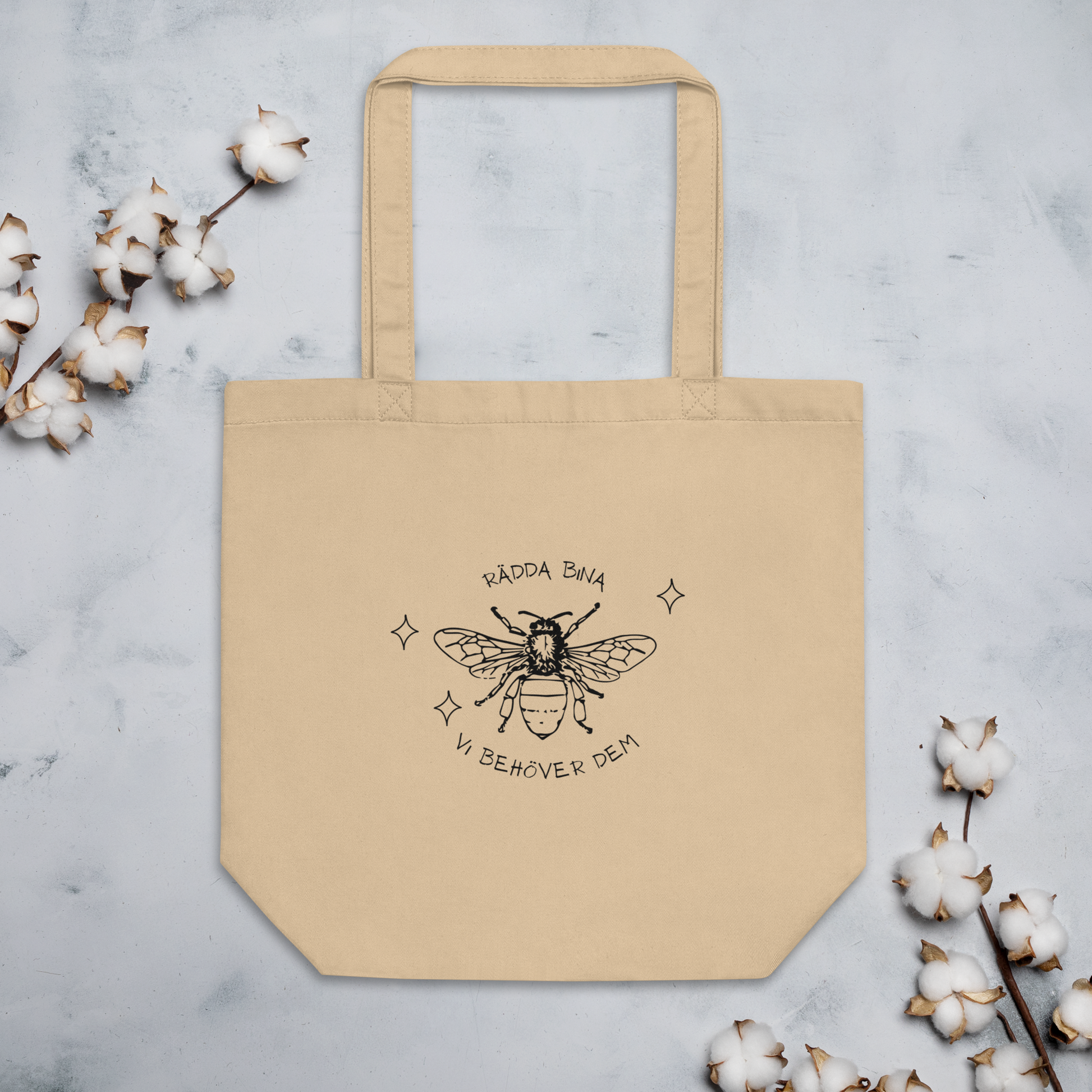 Naturfärgad beige ekologisk tygväska med svart handritat bi och texten "Rädda bina – vi behöver dem" runtom.
Natural-colored oyster organic tote bag with a black hand-drawn bee and the text "Rädda bina – vi behöver dem" surrounding it.