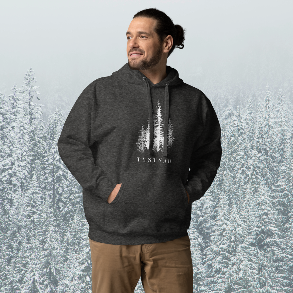 Mörkgrå melerad unisex premium hoodie med tryckta granar och texten Tystnad. Charcoal heather unisex premium hoodie with printed pine trees and the word  "Tystnad" on the chest.