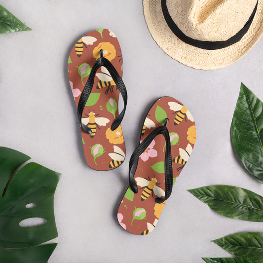 Flip-flops med tecknade bin och blommor på brun bakgrund.
Flip-flops with illustrated bees and flowers on a brown background.