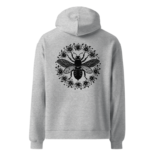 Unisex oversized hoodie i grått med ett stort bi- och blommotiv tryckt på ryggen, visad bakifrån.
Unisex oversized grey hoodie with a large bee and floral print on the back, shown from behind