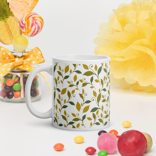 Vit blank keramikmugg 11 oz med grönt och gult lövmotiv runt om.
White glossy ceramic mug 11 oz with green and yellow leaf motif all around.